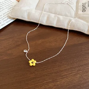 Close-up of silver-tone chain necklace with yellow flower pendant and zircon detail on wood