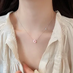 Close-up view of a delicate silver necklace featuring a pink flower pendant worn by a model