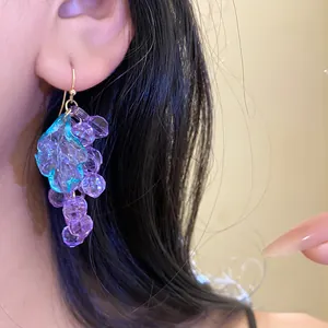 Close-up detail showing purple faceted acrylic grape earrings with a teal leaf