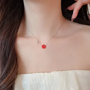 Close-up of a silver necklace featuring a red flower pendant and a sparkling zircon charm.