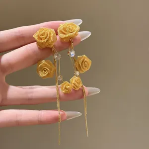 Detailed view of golden fabric rose earrings with zircon accents and long tassels