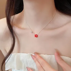 Close-up detail of a delicate silver chain necklace featuring a red flower pendant and zircon