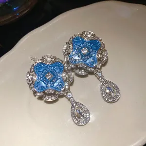 Macro view of blue enamel flower earrings with sparkling clear waterdrop pendants