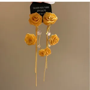 Detail of yellow fabric rose earrings with zircon accents and long gold tassels.