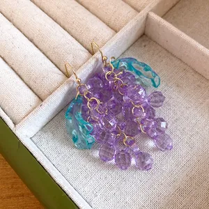 Close-up of purple acrylic grape earrings with teal leaves in a jewelry box