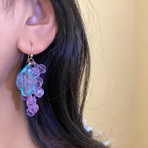 Detailed close-up view of purple acrylic grape earrings with leaf accent on a model's ear