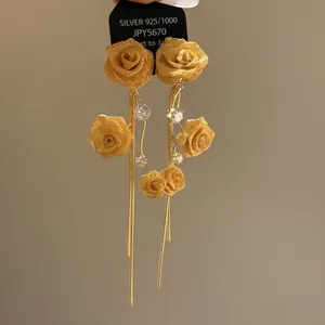 Detailed view of elegant golden fabric rose earrings with long tassels and zircons.
