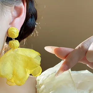 Detail of Bohemian yellow chiffon flower tassel earrings worn on ear with soft lighting