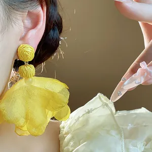 Close-up of yellow chiffon flower tassel earrings with boho style on model's ear