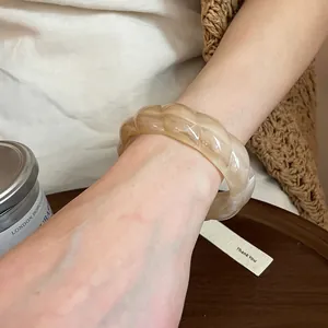 Close-up detail of a beige swirled resin twisted bangle worn on a female wrist