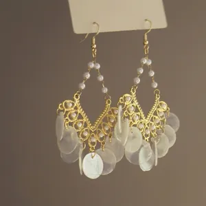 Detailed close-up of bohemian style gold earrings with white shell discs and pearls.