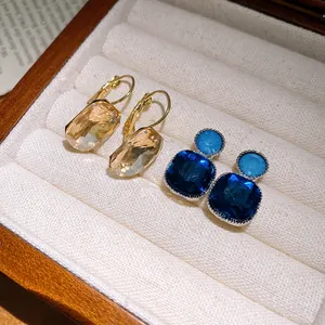 Close-up of champagne rectangular and blue square crystal earrings in a jewelry box