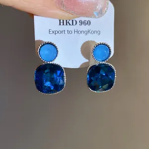 Macro detail showing blue crystal square pendant earrings mounted on white display card.