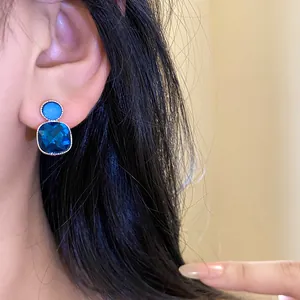 Macro view of elegant blue square crystal earrings with silver post worn by an Asian model