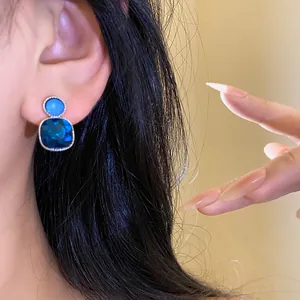 Close-up view of elegant blue square gemstone earring with silver needle and diamond accents