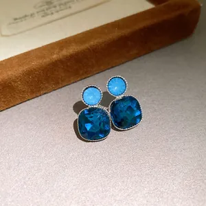 Detailed view of silver stud earrings with vibrant blue square and round crystals.