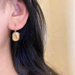 Detailed view of a square champagne crystal drop earring worn on a female ear model