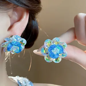 Detailed view of sparkling blue crystal flower stud earrings on a female model's ear