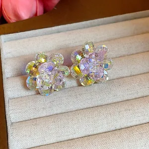 Close-up detail of iridescent glass flower stud earrings displayed in a beige jewelry box