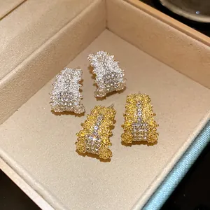 Close-up of elegant gold and silver C-shaped earrings with sparkling diamond-set textures