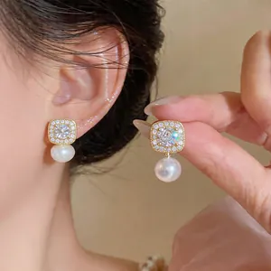 Close-up detail of vintage gold square stud earrings with elegant dangling white pearls