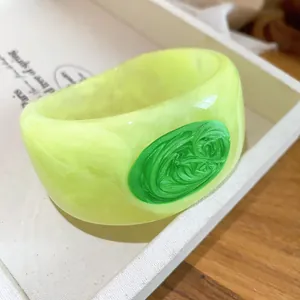 Close-up of chunky resin bangle with marbled yellow texture and green swirly oval detail.