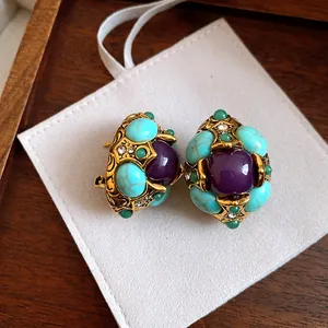 Close-up of vintage royal style gold earrings with purple and turquoise resin stones.