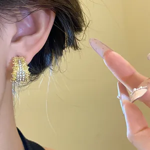 Close-up of a textured C-shaped gold earring with sparkling rhinestones worn on the ear