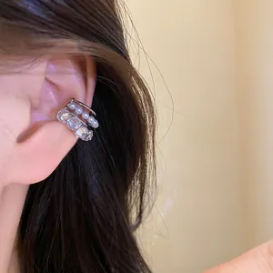 Detailed view of a silver ear cuff with pearls and zircons worn on model's ear.