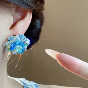 Close-up of sparkling blue iridescent glass flower stud earrings worn on human ear