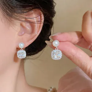 Close-up detail of elegant silver earrings with pearls and square halo zirconia stones.