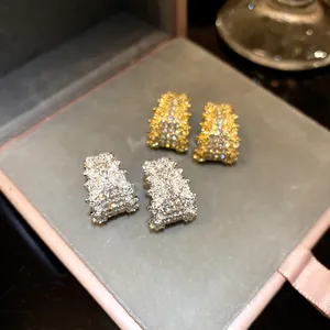 Close-up of sparkling C-shaped silver needle stud earrings in gold and silver colors