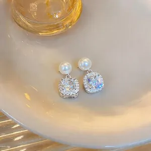 Elegant vintage square crystal halo earrings with white pearl drops on a ceramic plate