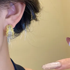 Detailed view of C-shaped gold stud earrings with rhinestones on model's ear