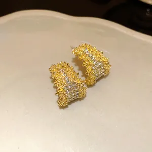 Macro view of gold C-shaped stud earrings with sparkling rhinestones and textured finish.