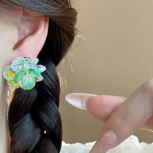 Close-up detail of iridescent green and yellow glass flower stud earrings worn on ear