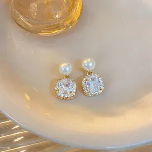 Close-up of elegant pearl earrings with sparkling square-cut zircon drops and gold trim