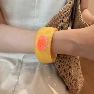 Detailed view of a chunky yellow resin bangle with a vibrant orange marbled swirl pattern.