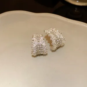 Close-up detail of C-shaped silver earrings with sparkling rhinestone encrustation
