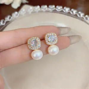 Close-up of vintage gold stud earrings featuring halo crystals and elegant white pearl drops