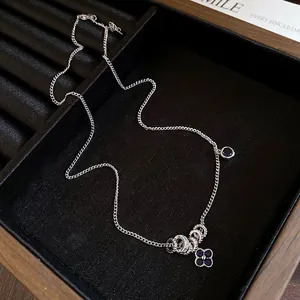 Detailed view of a silver necklace with blue zircon flower and ring charms on black tray
