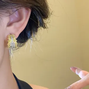 Elegant C-shaped gold-toned earrings with sparkling rhinestone details shown on ear.