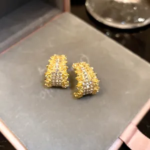 Detailed view of elegant C-shaped golden earrings encrusted with sparkling rhinestones.