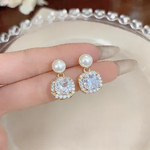 Close-up of elegant gold earrings with white pearls and square crystal pendants