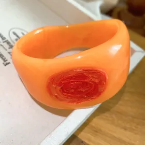 Close-up shot of a chunky orange resin bangle featuring a vibrant red marbled texture detail