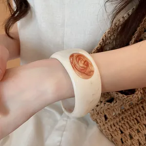 Close-up of a stylish wide resin bangle with a marbled orange drip oil inlay worn on wrist