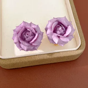 Detailed macro view of elegant purple rose flower stud earrings on a beige jewelry tray