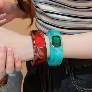 Stylish gradient resin bangles featuring large emerald-cut red and green gemstones.