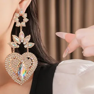 Close-up of oversized rhinestone heart earrings with aurora crystals and floral studs.