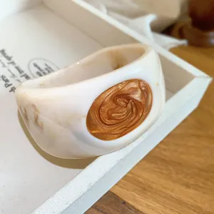 Detailed view of a thick marbled cream resin bangle with a decorative gold swirl oil-drop inlay